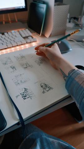 A person sitting at a desk with a pencil, drawing.