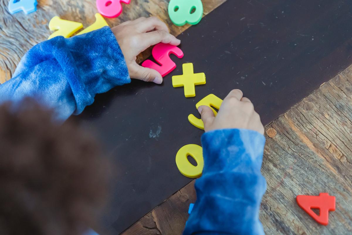 A child in a blue long-sleeved shirt plays with numbers on a table.