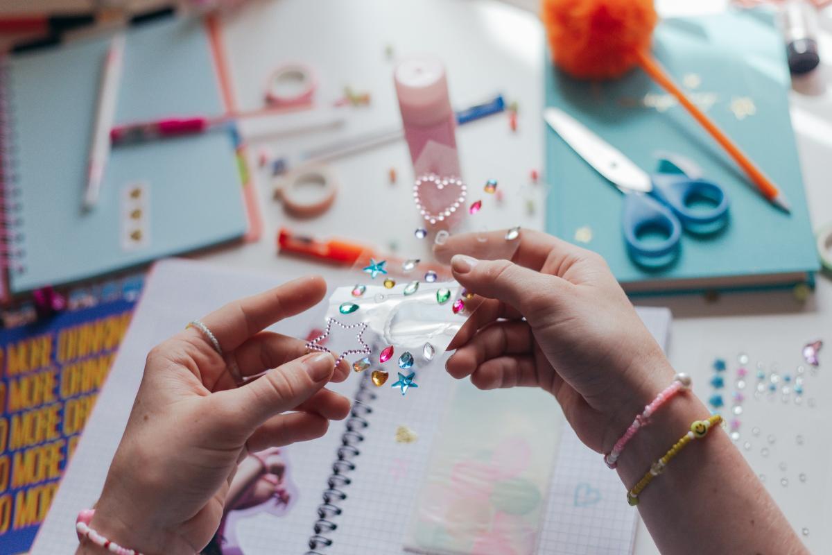 A person holds stickers, in front of a background filled with other craft supplies.