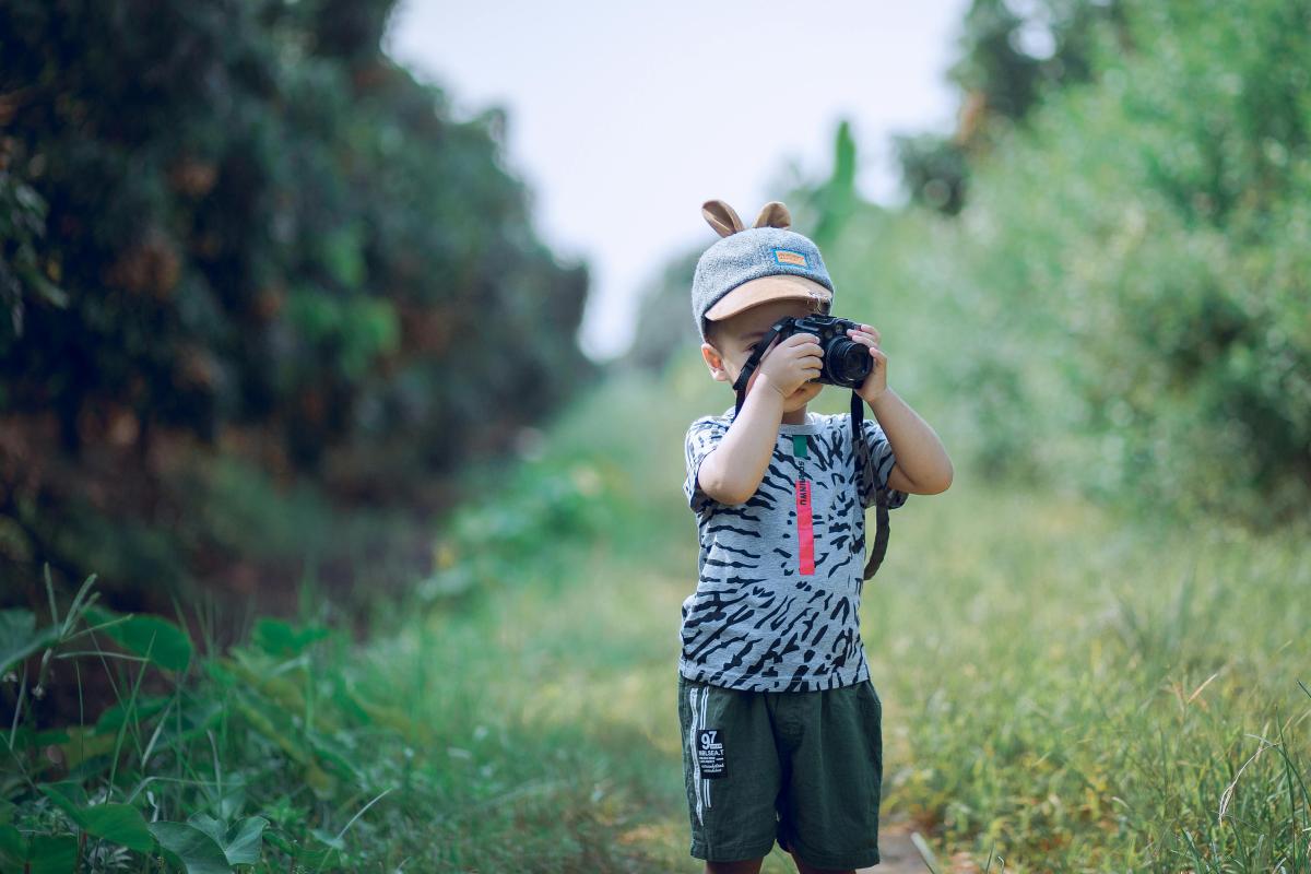 A young child is in a field looking through a camera.