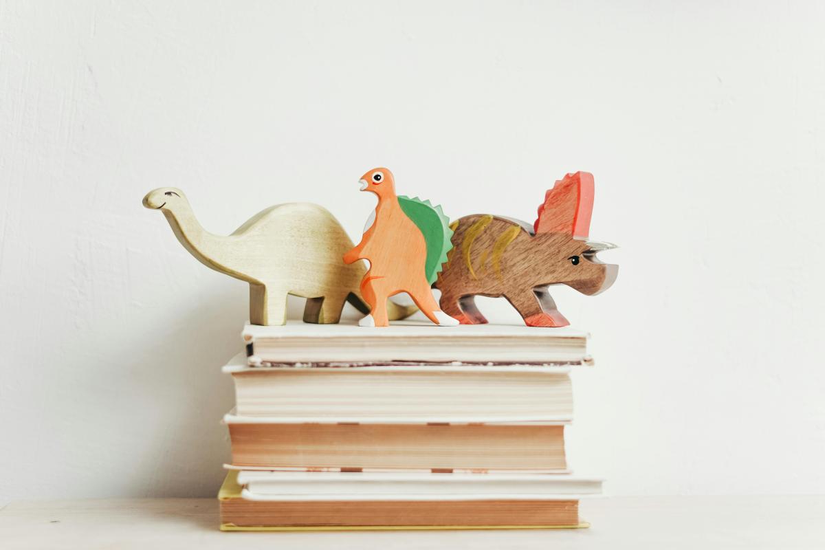 Three wooden dinosaurs on stack of books